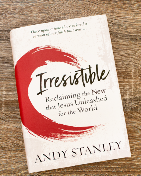 Book cover of "Irresistible" by Andy Stanley on wooden surface, white background with red circular brush stroke and subtitle "Reclaiming the New that Jesus Unleashed for the World."