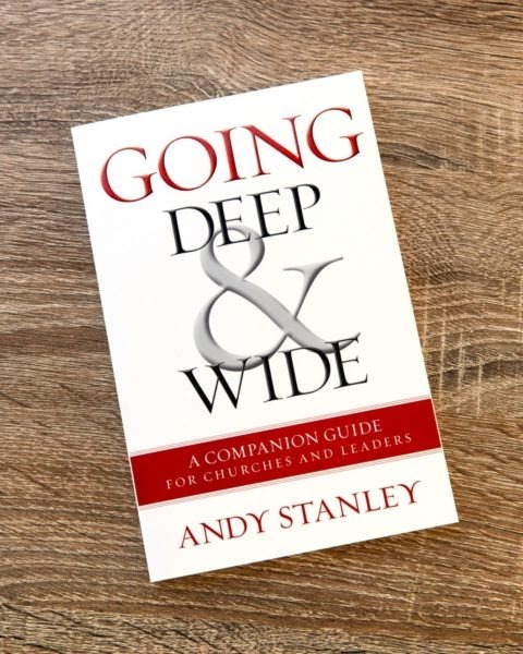 Book cover of "Going Deep &amp; Wide" by Andy Stanley on wooden surface, white background with red and black ampersand design and subtitle "A Companion Guide for Churches and Leaders."